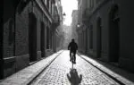 Fietser op Europese kasseienstraat met dramatische schaduwen en contrastrijke architectuur in zwart-wit sfeer