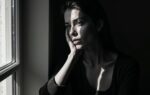 Vrouw gefotografeerd met extreem zijlicht vanuit een raam, waarbij de helft van haar gezicht in diepe schaduw valt en de andere helft scherp belicht is, zwart-wit portret met sculpturaal effect