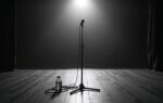 Verlaten podium na een concert in zwart-wit met een microfoonstandaard onder een spotlicht en achtergelaten kabels op het houten vloeroppervlak