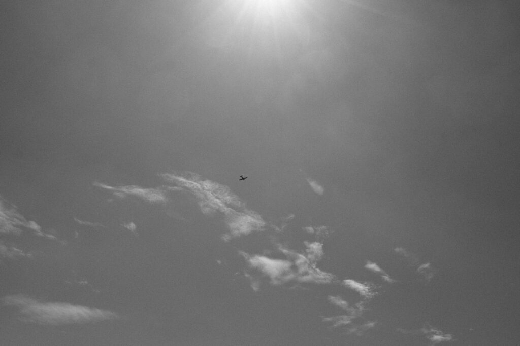Klein vliegtuig in de lucht met zon en wolken, zwartwit