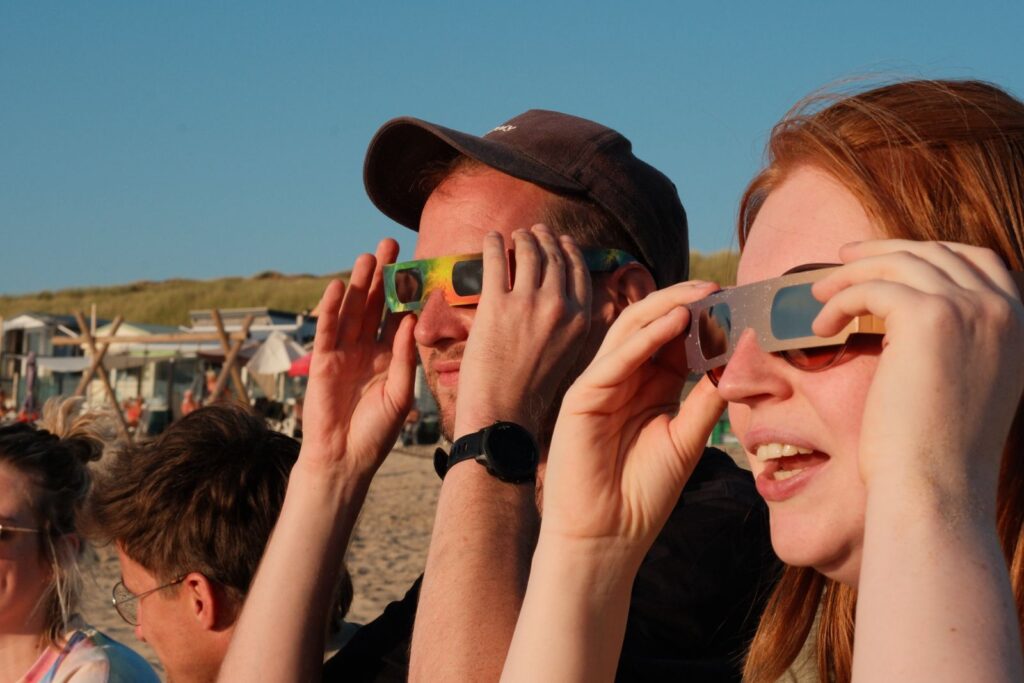 Zonsverduistering mensen kijken op het strand met een brilletje naar de zon